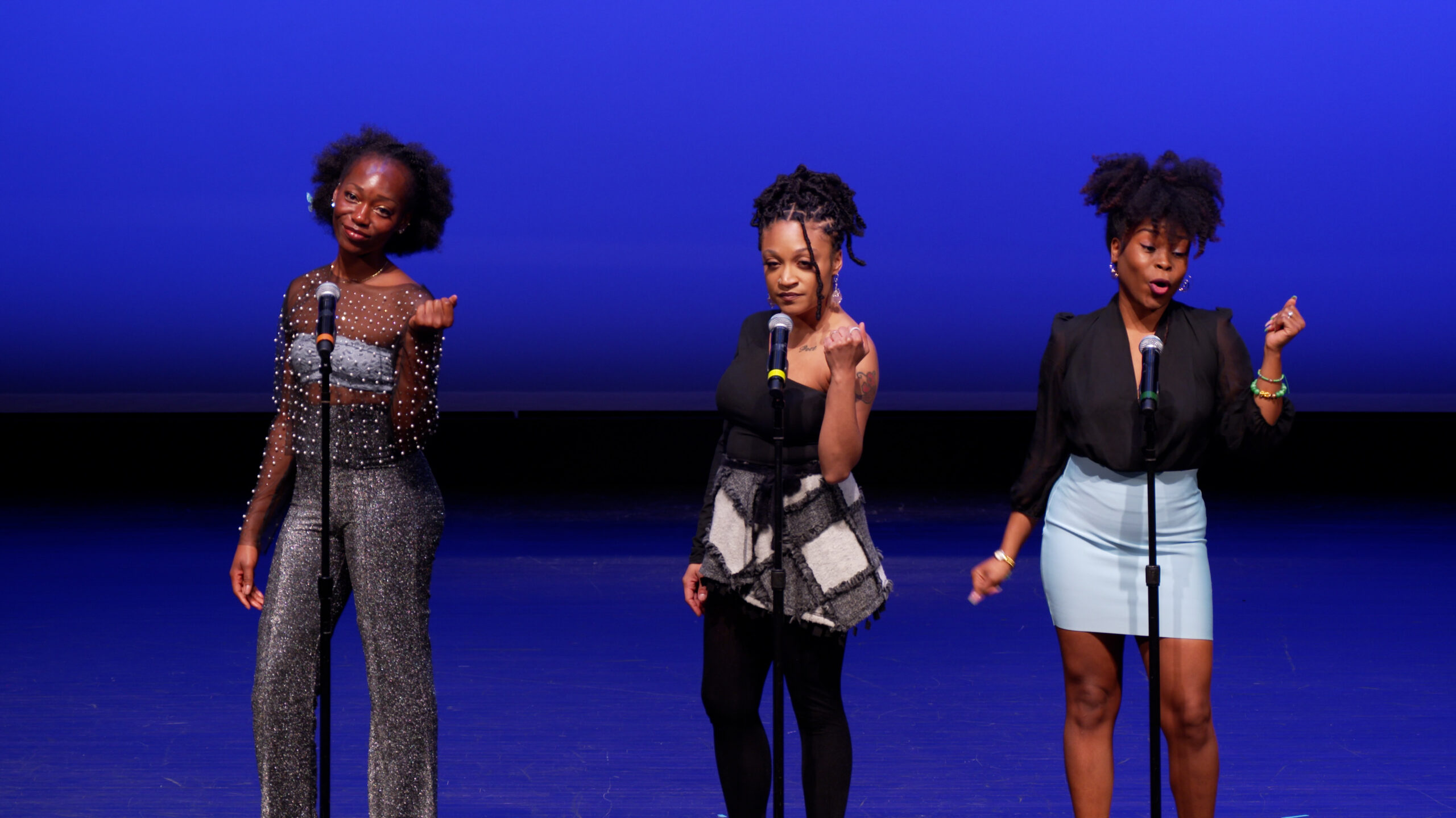 The Nuyorican Slam Team performs onstage at Dodge Poetry Festival. Three spotlit poets stand with microphones against a deep blue background.