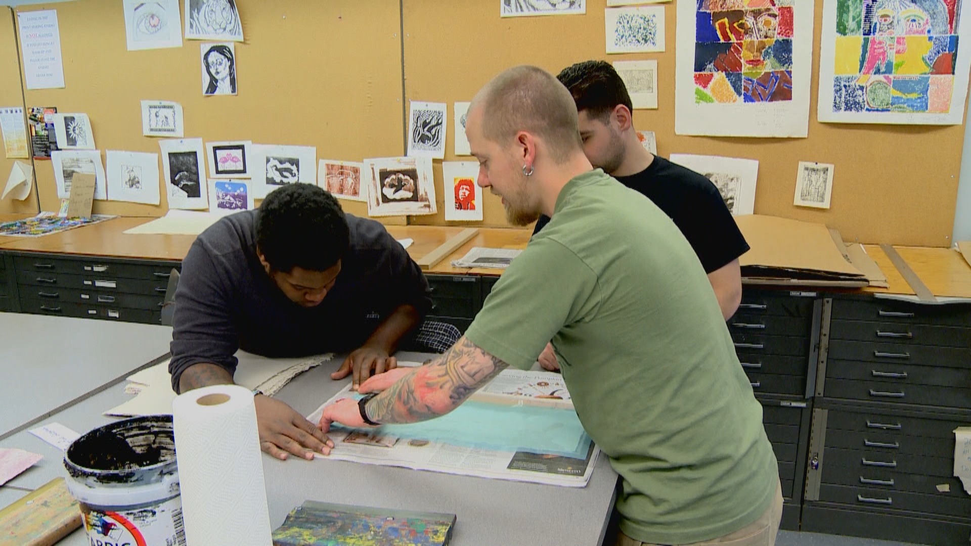 Three people work in an art studio to make homemade paper out of military uniforms at a Combat Paper workshop.