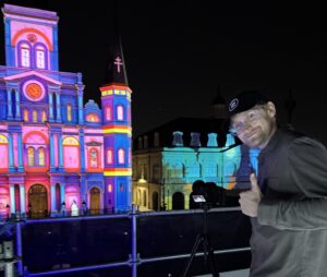 Videographer Jack Stawowczyk stands with a thumbs up smiling at the camera on location in New Orleans