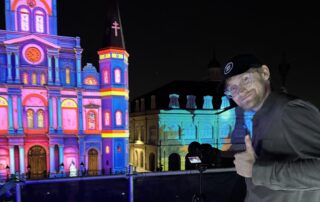 Videographer Jack Stawowczyk stands with a thumbs up smiling at the camera on location in New Orleans